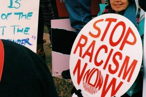 Person holding a sign which reads, "Stop Racism Now."