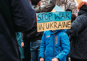 Child holding sign in a crowd that reads 'Stop war in Ukraine'