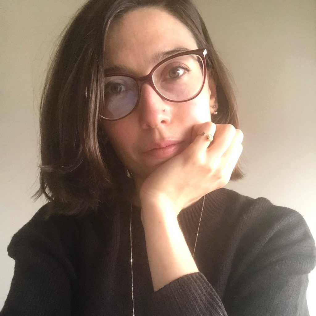 Bursa Headshot, short brunette hair, brown glasses, brown eyes, wearing a black sweater and has her hand under her chin
