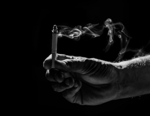 The Smoking Epidemic and the Pandemic Black and white photo of a hand holding a lit cigarette